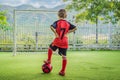 Little cute kid boy in red football uniform playing soccer, football on field, outdoors. Active child making sports with