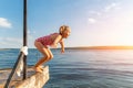 Little cute kid girl in swimsuit have fun enjoy pretend flying jumping from pier dock in clean blue water sea river or