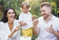 Little cute kid and his parents are tasting festive cake outdoors in garden. Happy family having fun Royalty Free Stock Photo