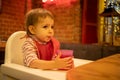 A little cute kid sits in a highchair, holds a glass of juice with his hands and drinks from a straw. in the background Royalty Free Stock Photo