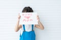 Little cute little girl with curly hair holding handmade card with text Love Mom, showing card cover her face Royalty Free Stock Photo