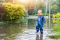 Little cute playful caucasian blond toddler boy enjoy have fun playing jumping in dirty puddle wearing blue waterproof Royalty Free Stock Photo