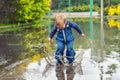 Little cute playful caucasian blond toddler boy enjoy have fun playing jumping in dirty puddle wearing blue waterproof Royalty Free Stock Photo