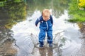 Little cute playful caucasian blond toddler boy enjoy have fun playing jumping in dirty puddle wearing blue waterproof Royalty Free Stock Photo