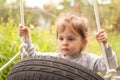 Little cute red-haired girl riding a black wheel swing tied with ropes on a hot summer day outdoors Royalty Free Stock Photo