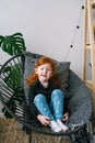 Little cute redhead girl in jeans sit in armchair. Surprised emotions Royalty Free Stock Photo