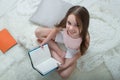 Little cute smiling girl reads books sitting on her bed. Top view