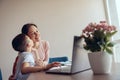 Little cute son kissing his mother in cheek while studying online at laptop at home. Royalty Free Stock Photo