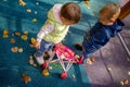 Little cute toddler boy and a beautiful year-old baby girl in blue clothes play in a pink toy stroller for a doll in the