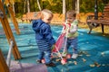 Little cute toddler boy and a beautiful year-old baby girl in blue clothes play in a pink toy stroller for a doll in the