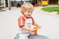Little cute toddler boy playing with car and tractor toys outdoors. Happy baby child playing at playschool or