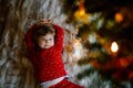 Little cute toddler girl lies under Christmas tree and dreaming of Santa at home, indoors. Traditional Christian Royalty Free Stock Photo