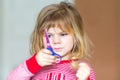 Little cute toddler girl making experiment with scissors and cutting hairs. Funny baby child cuts her pony herself at