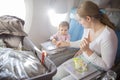 A little cute toddler girl sitting in an airplane in a chair at the porthole wipes with her mother a folding table with
