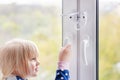 Little cute toddler girl trying to open window in apartment at high-tower building. Children window protection lock. Cable safety Royalty Free Stock Photo