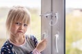 Little cute toddler girl trying to open window in apartment at high-tower building. Children window protection lock Royalty Free Stock Photo