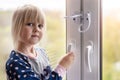 Little cute toddler girl trying to open window in apartment at high-tower building. Children window protection lock Royalty Free Stock Photo