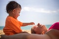 Little cute toddler is playing and pestering mom who is lying on the sand of a beach. warm sea on a sunny day in the background Royalty Free Stock Photo