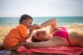 Little cute toddler is playing and pestering a young Caucasian mom who is lying on the sand of a beach. warm sea on a