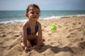 Little cute toddler tanned Caucasian girl in a blue swimsuit sitting on a sandy beach against the background of sea waves Royalty Free Stock Photo