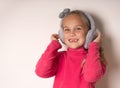 Little cute toothless girl fooling around in warm fur headphones on a light background.