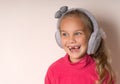 Little cute toothless girl fooling around in warm fur headphones on a light background.