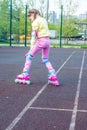 A little cute white girl in a yellow sweatshirt and pink jeans on roller skates in the park. Learn to rollerblade