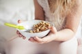 Little cute white-haired girl eats granola on the bed in her bright room. Healthy food. Home comfort Royalty Free Stock Photo