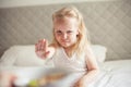 Little cute white-haired girl eats granola on the bed in her bright room. Healthy food. Home comfort Royalty Free Stock Photo