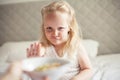 Little cute white-haired girl eats granola on the bed in her bright room. Healthy food. Home comfort Royalty Free Stock Photo