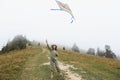 Little cute 7 years old girl playing with colorful kite on foggy day in the mountains. happy child in green jumpsuit and Royalty Free Stock Photo