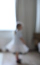 little dancing ballerina girl out of focus indoors. Little Caucasian girl in babydoll dress standing by big window Royalty Free Stock Photo