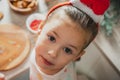 Little dark-haired girl 3 years old in Santa hair band looks up at camera in kitchen. Merry Christmas. Happy New Year Royalty Free Stock Photo