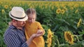 The little daughter in arms of the farmer's dad looks at sunflower flower in field in the rays of the beautiful sun. A Royalty Free Stock Photo