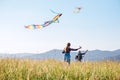 Little daughter with the father running fast while they flying up colorful kites on the high grass meadow in the mountain fields.