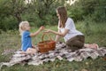 Little daughter gives apples her Young mother, on clearing in forest. Summer picnic of mom and girl on plaid blanket