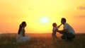 Little daughter goes from mom to dad, hugs and kisses her parents in rays of a warm sun. Happy family walks in park at Royalty Free Stock Photo