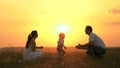 Little daughter goes from mom to dad, hugs and kisses her parents in rays of a warm sun. Happy family walks in park at Royalty Free Stock Photo