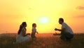 Little daughter goes from mom to dad, hugs and kisses her parents in rays of a warm sun. Happy family walks in park at Royalty Free Stock Photo