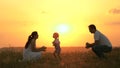 Little daughter goes from mom to dad, hugs and kisses her parents in rays of a warm sun. Happy family walks in park at Royalty Free Stock Photo