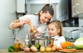 Daughter helping cooking soup and mother add pepper to pan Royalty Free Stock Photo