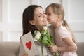 Little daughter kissing mother on cheek, presenting flowers and gift Royalty Free Stock Photo