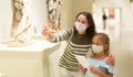 Little daughter and mother in protective masks inspect the exhibits in museum
