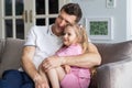 A little daughter sits on the sofa in the room together with father, who hugs her. A dad and child relax, spend leisure Royalty Free Stock Photo