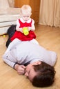 Little daughter sitting on the back of tired father lying unconscious on floor, man sleeping after playing toys with child Royalty Free Stock Photo