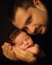 Little 15 days old baby lying securely on his Dad`s arms, against a black background Royalty Free Stock Photo