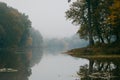 Little desolate natural lake on early misty autumn morning, old linden tree reflections on still water surface, green countryside