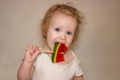 A little disheveled blue-eyed girl baby in white body tastes candy on a stick, a lollipop Royalty Free Stock Photo