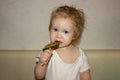 A little disheveled blue-eyed girl baby in white body tastes candy on a stick, a lollipop