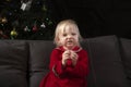 Little disheveled girl in a red dress sits on the sofa against the background of a Christmas tree. Christmas and new year`s eve